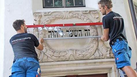 Steffen Voigt und Robin Habermann bringen über dem Eingang der St.-Nikolaus-Kapelle die Glasplatte mit dem ursprünglichen Text der dort befindlichen Sandsteinkartusche an.  Foto: Martin Koch