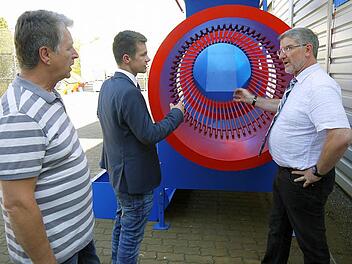 Ein bisschen auffallen darf schon sein: Die kräftigen Farben gehören bei der Brennholz-Reinigungstrommel dazu, erklären Norbert Dressel und Dominic Dressel Landrat Michael Busch bei der Führung durch das Außengelände des Metallbauspezialisten. Foto: Berthold Köhler