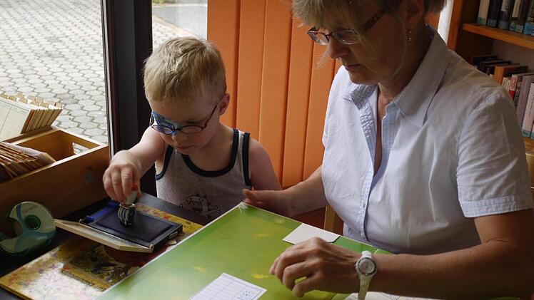Hannes Lösch darf Marita Römer beim Abstempeln der Bücher helfen (linkes Bild). Sigrid Lösch (r.) berät Ursula Oesterer bei der Buchauswahl.   Fotos: Pauline Lindner