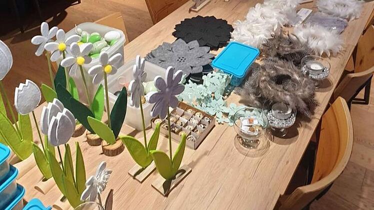Dekorative Artikel wie Filzblumen und Glasbehälter sind auf einem Tisch arrangiert. Der Raum hat Holzböden und Sitzmöglichkeiten, vorbereitet für einen Inventarverkauf.