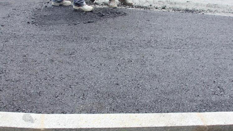 Zwei Bauarbeiter suchen einen unter dem Asphalt verschwundenen Wasserschieber. Dessen Lage im Schotter ist am Bordstein markiert.  Foto: Friedwald Schedel