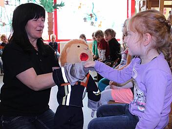 Sigrid Mager (Kreisbrandmeister) begrüßt mit Handpuppe Flori jedes Kind persönlich, hier gerade Arina. Die Kinder sollen lernen, dass Feuerwehrleute wichtige Helfer sind.