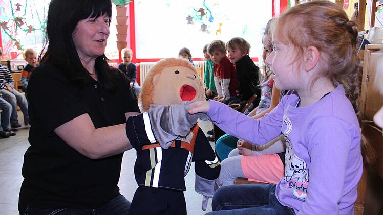 Sigrid Mager (Kreisbrandmeister) begrüßt mit Handpuppe Flori jedes Kind persönlich, hier gerade Arina. Die Kinder sollen lernen, dass Feuerwehrleute wichtige Helfer sind.