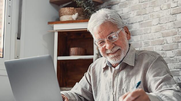 Älterer Fernarbeiter. Konzentrierte ältere männliche Person mit Brille. Arbeit am Laptop von zu Hause. Alter Mann Mitarbeiter. Home Office. Arbeiten trotz Rente.