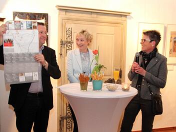 Bürgermeister Fischkal zeigt die Rückseite der Kunstkarte, daneben Siggi Wolt und Jutta Köhler. Fotos: Blum