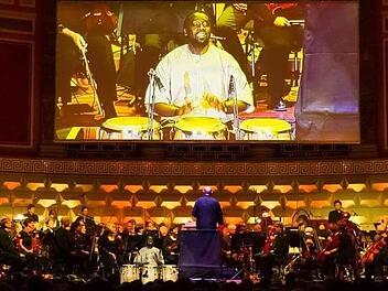 Hier trommelt Niang Serigne auf einer großen Bühne und unterstützt das Orchester mit seiner Kunst. Sein Foto wird auf einer großen Leinwand übertragen. Foto: Biggi Trost