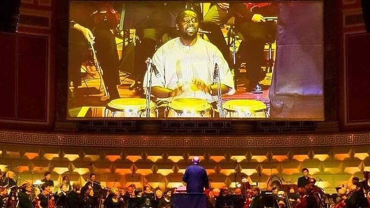 Hier trommelt Niang Serigne auf einer großen Bühne und unterstützt das Orchester mit seiner Kunst. Sein Foto wird auf einer großen Leinwand übertragen. Foto: Biggi Trost