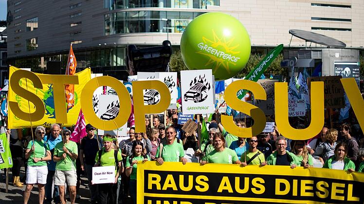 Frankfurt/Main: Demonstranten von Greenpeace stehen mit einem Transparent mit der Aufschrift «Raus aus Diesel und Benzin», dahinter fordern Demonstranten mit großen gelben Buchstaben «Stop SUV». Ist die Kritik an den SUV gerechtfertigt? Foto: Marius Becker/dpa