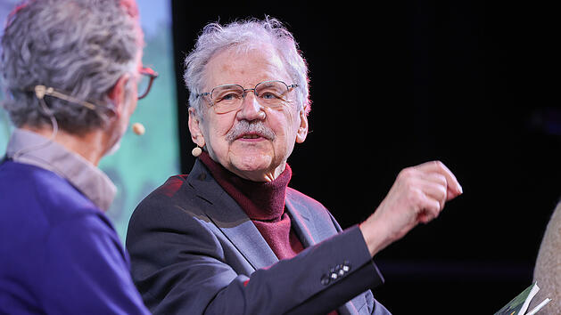 Zwei M&auml;nner diskutieren auf einer B&uuml;hne. Einer h&auml;lt ein Buch in der Hand. Beide tragen Mikrofone und scheinen in ein Gespr&auml;ch vertieft.