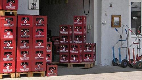 Im Bild sind gestapelte Bierk&auml;sten der Familienbrauerei Hennemann vor einem Geb&auml;ude zu sehen. Daneben stehen Handwagen. Die Brauerei ist in Sambach ans&auml;ssig.