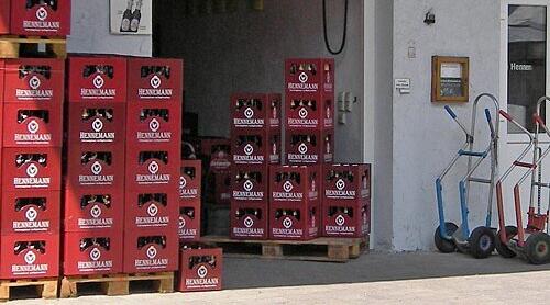 Im Bild sind gestapelte Bierk&auml;sten der Familienbrauerei Hennemann vor einem Geb&auml;ude zu sehen. Daneben stehen Handwagen. Die Brauerei ist in Sambach ans&auml;ssig.