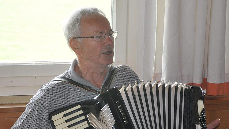 Musiker Rudi Fischer gibt mit dem Schifferklavier auf der Bank sitzend den Takt vor.