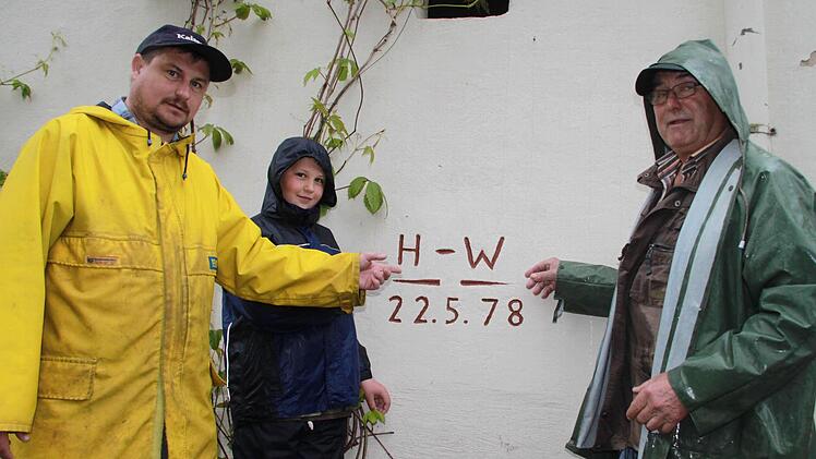 Armin, Markus und Erwin Fuß zeigen auf die Hochwassermarke von 1978, die diesmal in Prächting bei weitem nicht erreicht wurde. Foto: Matthias Einwag