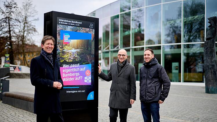 Projektleitung Sascha G&ouml;tz (von links), Referent f&uuml;r Wirtschaft und Digitalisierung Dr. Stefan Goller und Projektmanager Jonas Behr vor dem BamBoard an der Konzerthalle.