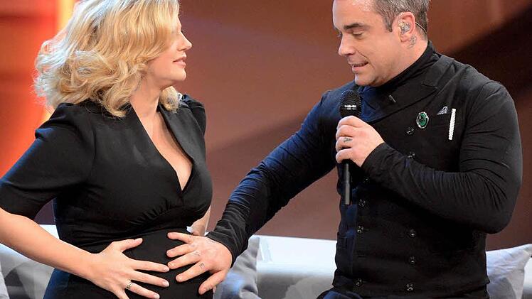 Robbie Williams legt am 03.11.2012 in der ZDF-Show &laquo;Wetten, dass..?&raquo; in der &Ouml;VB-Arena in Bremen seine Hand auf den Bauch der schwangeren Moderatorin Barbara Sch&ouml;neberger. Foto: Sascha Baumann/ZDF/dpa