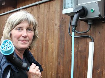 Margit Gutmair zeigt Ladekabel und Stromtankstelle im Garten. Die Steckdose am Auto ist vorne, der Tour-Report informiert. Foto: Waltraud Enkert