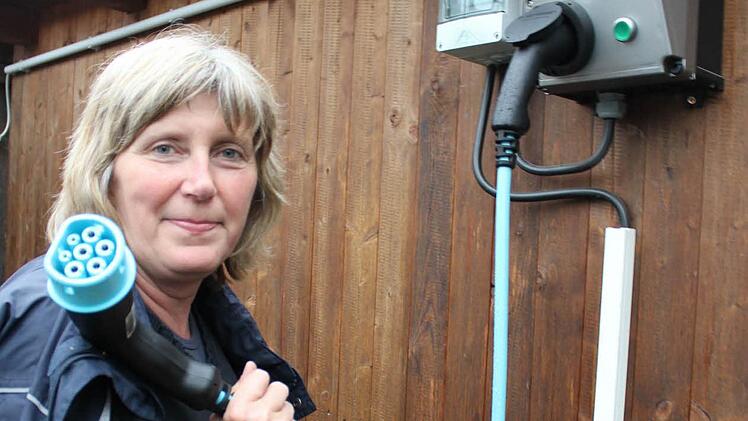 Margit Gutmair zeigt Ladekabel und Stromtankstelle im Garten. Die Steckdose am Auto ist vorne, der Tour-Report informiert. Foto: Waltraud Enkert