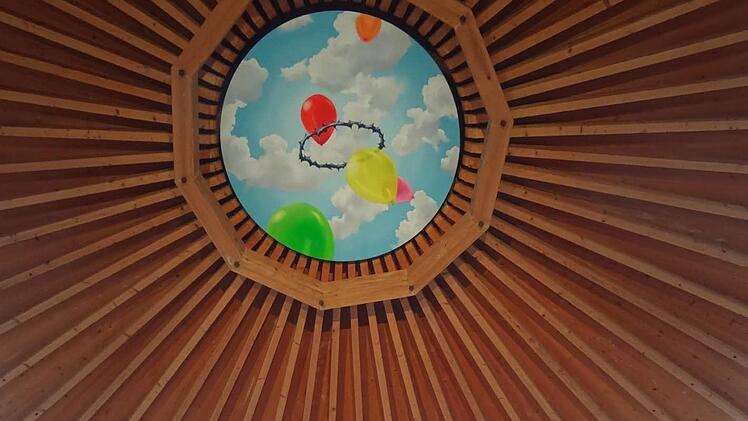 Der Kontrast zwischen der dunklen, spitzen Form der Dornenkrone und den farbendrohen Rundungen der Ballons als banalen Produkten der Spaßgesellschaft verweist auf einen Gegensatz: An der Realität von Leiden und Tod zerplatzen die Illusionen. Die bunte Welt der aufsteigenden Träume wird konfrontiert mit der Leidensgeschichte Jesu, der Theologie des Kreuzes. So liest man in der Begleitbroschüre zum Kunstwerk. Fotos Johanna Eckert