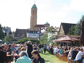 Eine Menschenmenge genießt ein Fest im Freien, sitzt an Biertischen. Im Hintergrund stehen Fachwerkhäuser und ein Kirchturm. Der Sonnenschein sorgt für eine fröhliche Atmosphäre.