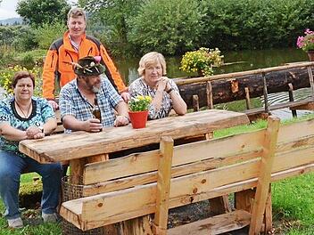 An dieser von Gerhard Deuerling (sitzend) geschaffenen Sitzgruppe lässt es sich gut entspannen. Mit im Bild Revierleiter Christian Goldammer und im Hintergrund der Dorfteich Foto: K.- H. Hofmann