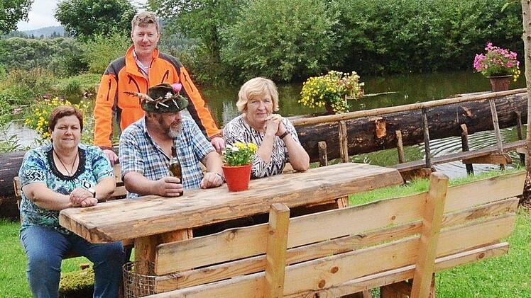 An dieser von Gerhard Deuerling (sitzend) geschaffenen Sitzgruppe lässt es sich gut entspannen. Mit im Bild Revierleiter Christian Goldammer und im Hintergrund der Dorfteich Foto: K.- H. Hofmann