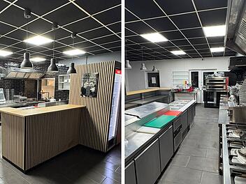 Moderne Pizzeria-Küche mit schwarzer Kachelwand, Edelstahlgeräten und Holztheke. Deckenbeleuchtung sorgt für helles Ambiente. Ideal für neue Filiale von "Abramo" in Oberhaid.