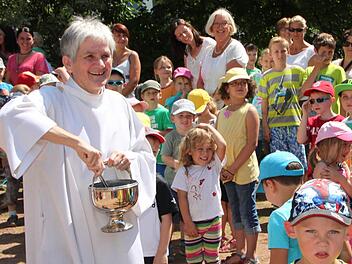 Erfrischende Segnung: Gemeindereferentin Johanna Schießl verteilt großzügig Weihwasser auf den neuen Spielgeräten - auch die Kinder bekommen ein paar Tropfen ab. Foto: Ulrike Müller