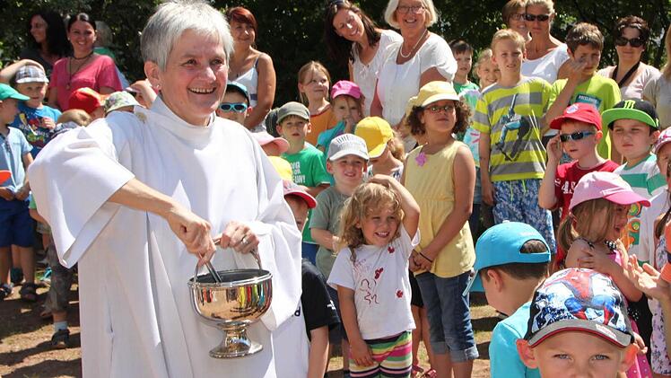 Erfrischende Segnung: Gemeindereferentin Johanna Schießl verteilt großzügig Weihwasser auf den neuen Spielgeräten - auch die Kinder bekommen ein paar Tropfen ab. Foto: Ulrike Müller