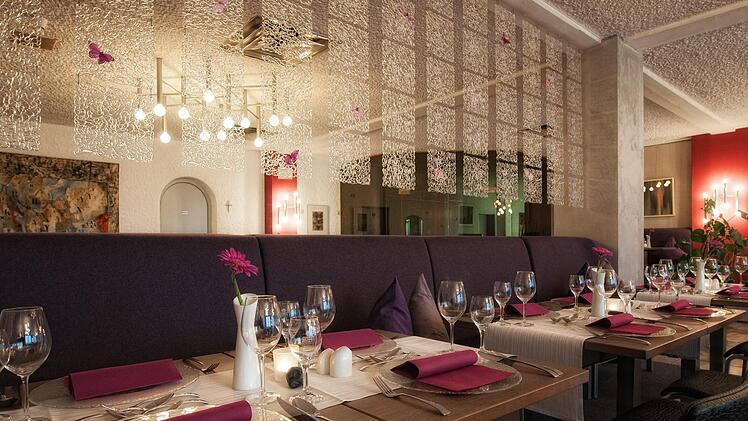 Elegantes Hotelrestaurant mit lila Akzenten und dekorativer Beleuchtung. Gedeckte Tische mit Weingläsern und stilvollen Details schaffen ein einladendes Ambiente für Gäste und Events.