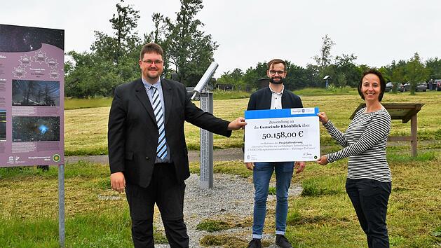 Ulrike Schade &uuml;bergab den symbolischen Scheck an B&uuml;rgermeister Christoph Friedrich. Schade und die Mitarbeiterinnen und Mitarbeiter aus der Th&uuml;ringer Verwaltung des Biosph&auml;renreservats (hier  Frank Riedel, Mitte) begleiten die Kommunen bei der Umsetzung der Projekte im Rahmen des F&ouml;rderprogramms. Auf der Fl&auml;che im Hintergrund wird der Sky-Pole errichtet.  Foto: Anna-Lena Bieneck