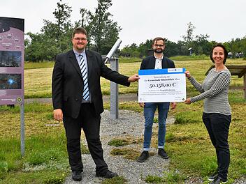 Ulrike Schade &uuml;bergab den symbolischen Scheck an B&uuml;rgermeister Christoph Friedrich. Schade und die Mitarbeiterinnen und Mitarbeiter aus der Th&uuml;ringer Verwaltung des Biosph&auml;renreservats (hier  Frank Riedel, Mitte) begleiten die Kommunen bei der Umsetzung der Projekte im Rahmen des F&ouml;rderprogramms. Auf der Fl&auml;che im Hintergrund wird der Sky-Pole errichtet.  Foto: Anna-Lena Bieneck