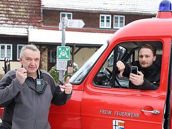 Mitten in Heiligkreuz gibt es zwar einen offiziellen Rettungstreffpunkt (Schild hinten), aber keinen Handy-Empfang: Feuerwehr-Kommandant Armin Henning (links) hat mit dem Digitalfunkgerät Empfang, während Daniel Niebusch (rechts), Vorsitzender der Wehr, mit dem Handy Pech hat. Foto: Ralf Ruppert/Archiv
