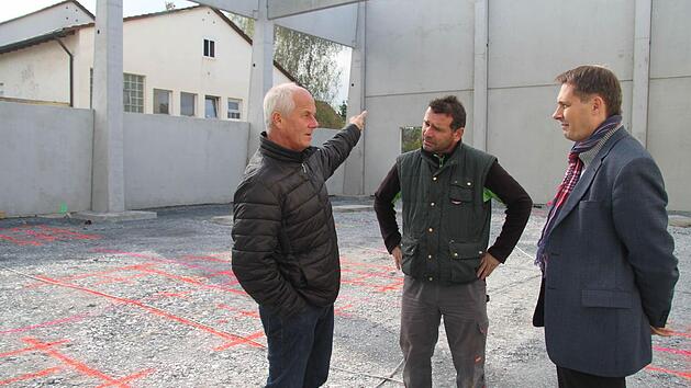 B&uuml;rgermeister Roland Wolfrum (rechts) und Schulleiter Michael Pfitzner (links) lie&szlig;en sich von Uwe Gruner (Mitte) den Fortschritt auf der Baustelle rund um die neue Turnhalle in Stadtsteinach erkl&auml;ren. Die rot eingezeichneten Linien im Hintergrund sind die Markierungen, in denen Vertiefungen eingearbeitet werden. Diese Vertiefungen sind f&uuml;r die Sportger&auml;te n&ouml;tig. Foto: Sonny Adam