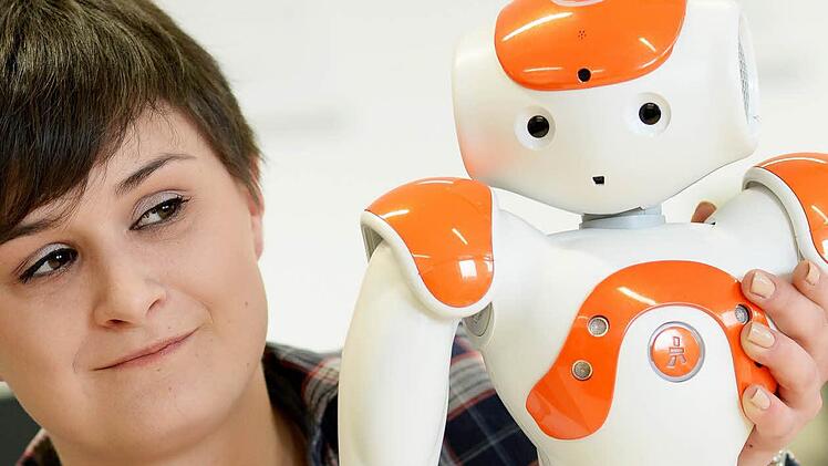 Simone Schineller, Studentin im Bereich "Angewandte Informatik" an der Otto-Friedrich-Universität Bamberg, mit einem humanoiden Roboter. Foto: David Ebener/dpa