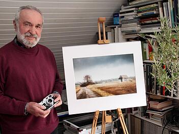 Der Künstler steht neben einem seiner Bilder, das durch die Windschutzscheibe fotografiert ist. Es zeigt das Grünseegebiet bei Adelsdorf. In der Hand hält er stolz eine alte Leica M2 aus dem Jahr 1960.  Fotos: Johanna Blum
