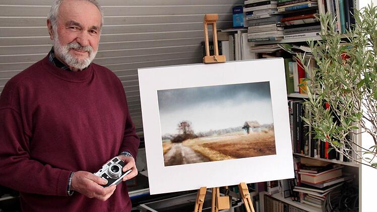 Der Künstler steht neben einem seiner Bilder, das durch die Windschutzscheibe fotografiert ist. Es zeigt das Grünseegebiet bei Adelsdorf. In der Hand hält er stolz eine alte Leica M2 aus dem Jahr 1960.  Fotos: Johanna Blum