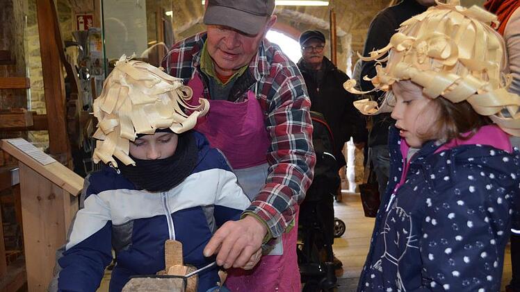 Gustav Luthardt zeigt Hannes und Pauline, was man alles aus Holz schnitzen kann. Foto: Gabi Bertram