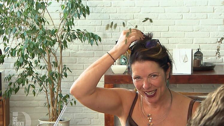 Wibke (53) verziert ihre Frisur am Tisch mit Zittergras.