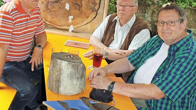 Die Autoren Harald Ostrow, Klaus Engelhardt und Mundartdichter Klaus Kempf (von links) betrachten die Relikte aus der Grüber Vergangenheit: die Baumscheibe der Kiefer, ein Stück Holzrohr und die schweren Bohrer, die zur Herstellung der alten Leitungen notwendig waren. Foto: Heinz Stammberger