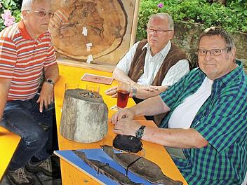 Die Autoren Harald Ostrow, Klaus Engelhardt und Mundartdichter Klaus Kempf (von links) betrachten die Relikte aus der Grüber Vergangenheit: die Baumscheibe der Kiefer, ein Stück Holzrohr und die schweren Bohrer, die zur Herstellung der alten Leitungen notwendig waren. Foto: Heinz Stammberger