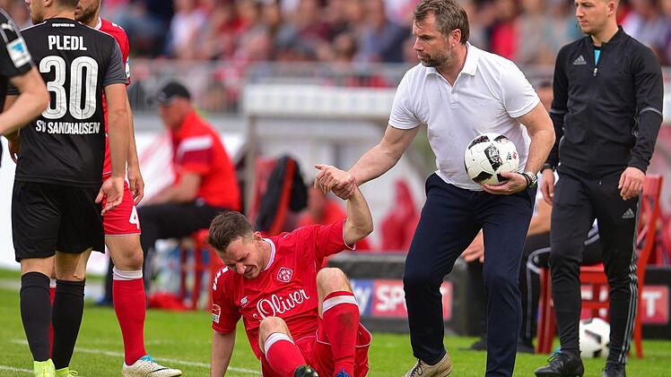 Immer wieder aufstehen: W&uuml;rzburgs Trainer Bernd Hollerbach (2.v.r.) holt nach einem Foulspiel den Ball und zieht seinen Spieler Peter Kurzweg (M) nach oben, um einen Zeitverlust zu vermeiden. Die W&uuml;rzburger Kickers sind nach der Pleite gegen Sandhausen auf den 17. Tabellenplatz abgerutscht. Foto: dpa