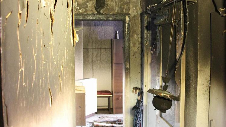 Die Haustür ist von der Hitze zerborsten. Der Blick vom Treppenhaus in die Unglückswohnung lässt erahnen, wie sehr das Feuer gewütet hat. Das Wohnzimmer, wo der Leichnam gefunden wurde, darf nicht betreten werden; es ist vollständig zerstört.