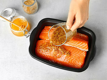 Woman preparing salmon fillet with honey mustard marinade in dis - Lachs