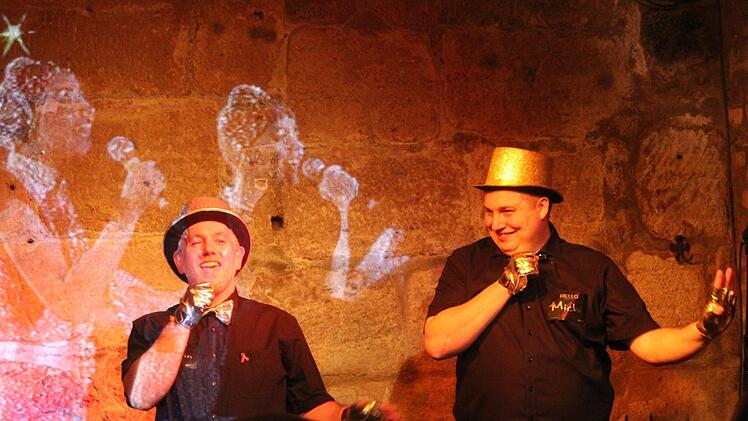 Martin Cla&szlig; (Uferlos-Vorsitzender, links) und Veranstalter Michael Behr er&ouml;ffnen den ESC-Abend in Bamberg mit einer Tanzperformance zum Lied "Hallo Welt" von Gitti und Erika (im Hintergrund zu sehen), mit dem das deutsche Gesangsduo beim Grand Prix 1983 in &Ouml;sterreich antrat.  Foto: M. Klein