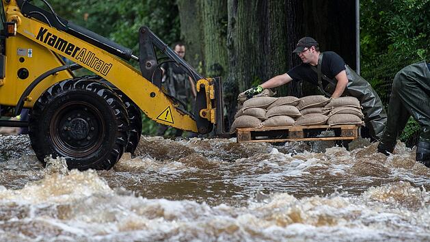 Feuerwehrmänner laden am 26.07.2017 in Holzminden (Niedersachsen) Sandsäcke von einem Radlader ab. Wie hier kam es in vielen teilen Deutschlands zu Überschwemmungen - und eine Entspannung der Lage ist erst einmal nicht in Sicht. Foto: Silas Stein/dpa