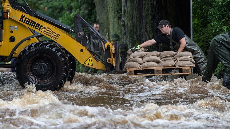 Feuerwehrmänner laden am 26.07.2017 in Holzminden (Niedersachsen) Sandsäcke von einem Radlader ab. Wie hier kam es in vielen teilen Deutschlands zu Überschwemmungen - und eine Entspannung der Lage ist erst einmal nicht in Sicht. Foto: Silas Stein/dpa