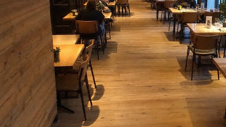 Ein Restaurant mit Holzboden, leeren Tischen, und vereinzelten G&auml;sten. Ein ruhiges Ambiente, das an den Ort eines k&uuml;rzlichen medizinischen Notfalls erinnert, bei dem Zivilcourage das Leben eines Mannes rettete.