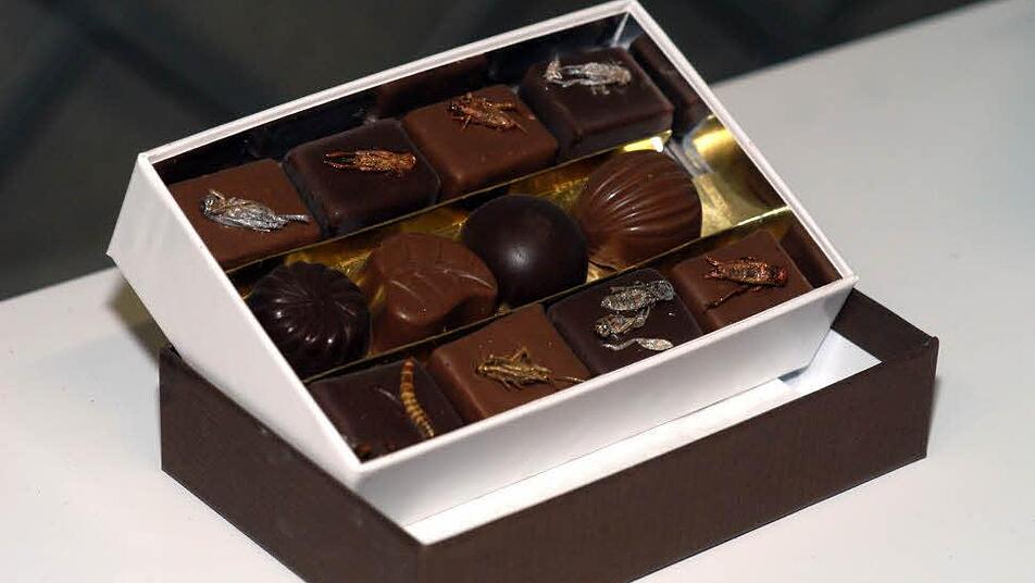 Manch einer gönnt sich sogar freiwillig den Genuss von Insekten: Eine Box mit Schokopralinen, die vom französischen Chocolatier Guy Roux mit Grillen und Mehlwürmern dekoriert wurden, Foto: dpa