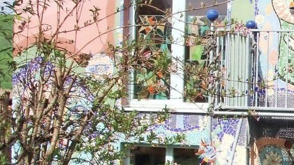 Frontansicht von Anne Huberths Villa Kunterbunt. Rechts: Wie flüssiges Gold scheint die Sonne durch die "Glasvorhänge".