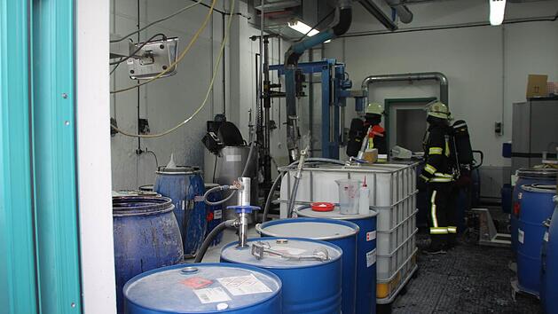 Schwerer Atemschutz: Feuerwehrleute mit Spezialausrüstung kontrollieren in der CoMI-Produktionshalle, ob immer noch Explosionsgefahr besteht. Links das Tintenfass und die Abfüllmaschine, wo es gebrannt hat. Foto: Stephan Tiroch